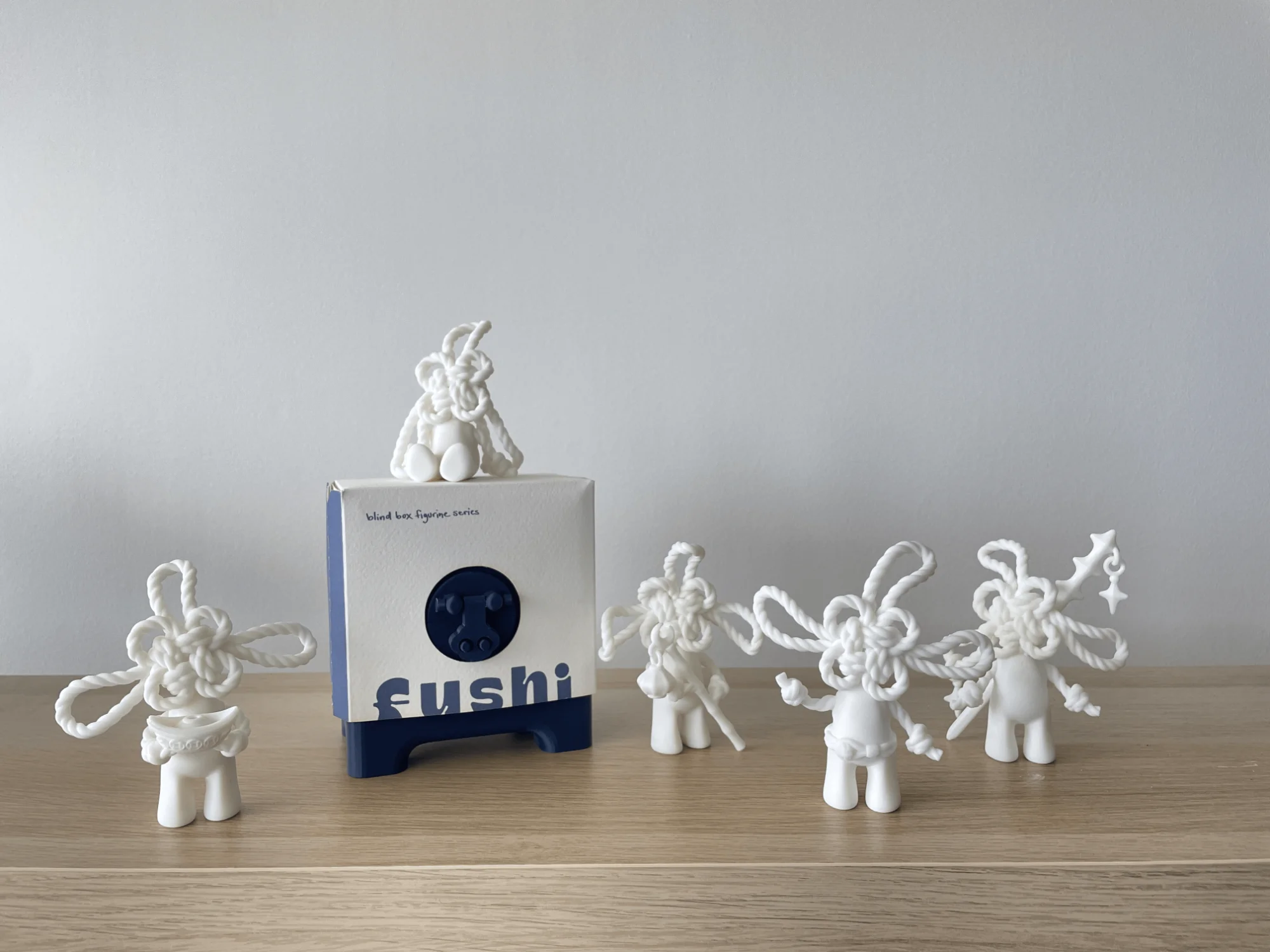 The final FUSHI box in its paper sleeve, with five resin figurines around it on a wooden table