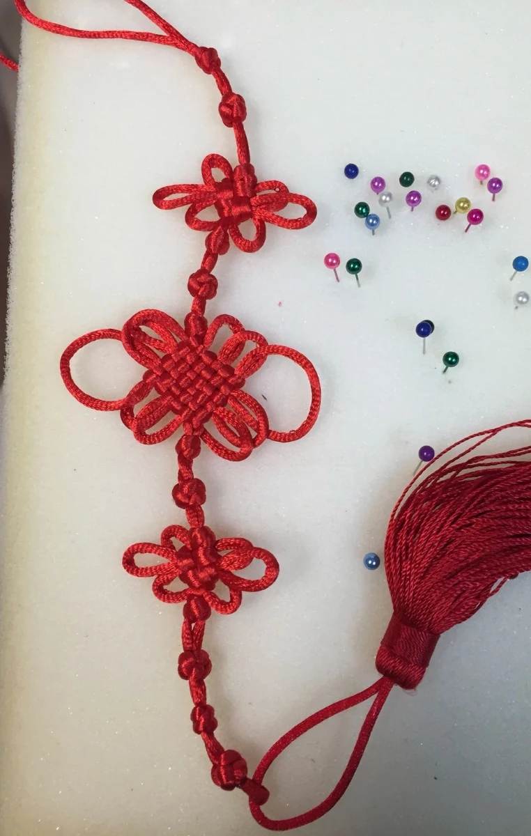 A red Chinese knot with looped petals and a tassel, pinned to foam
