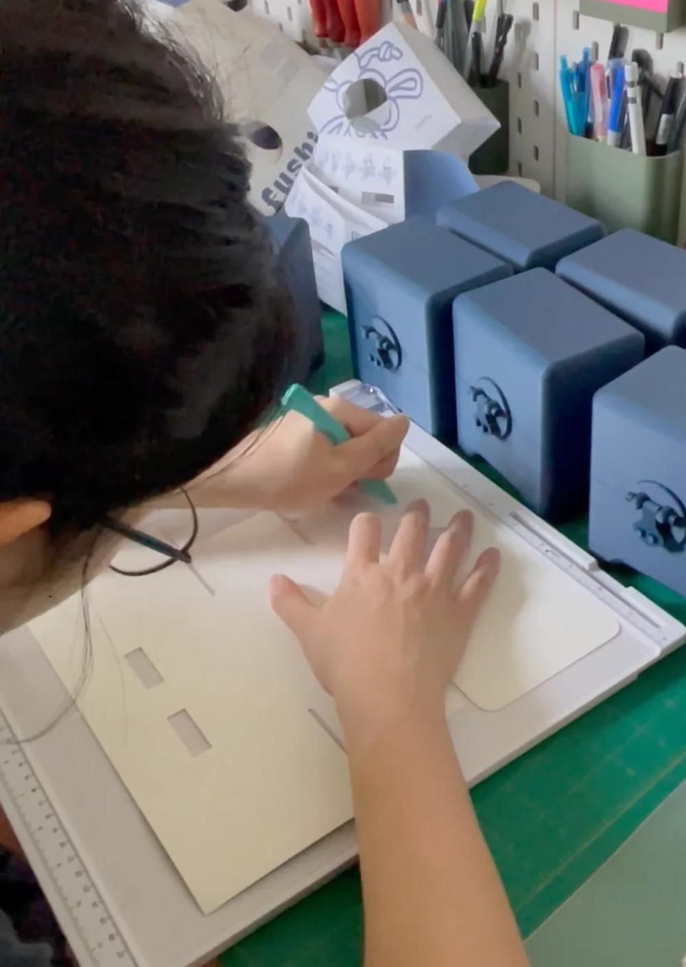 Scoring the laser-cut packaging on a score board, with blue printed boxes alongside