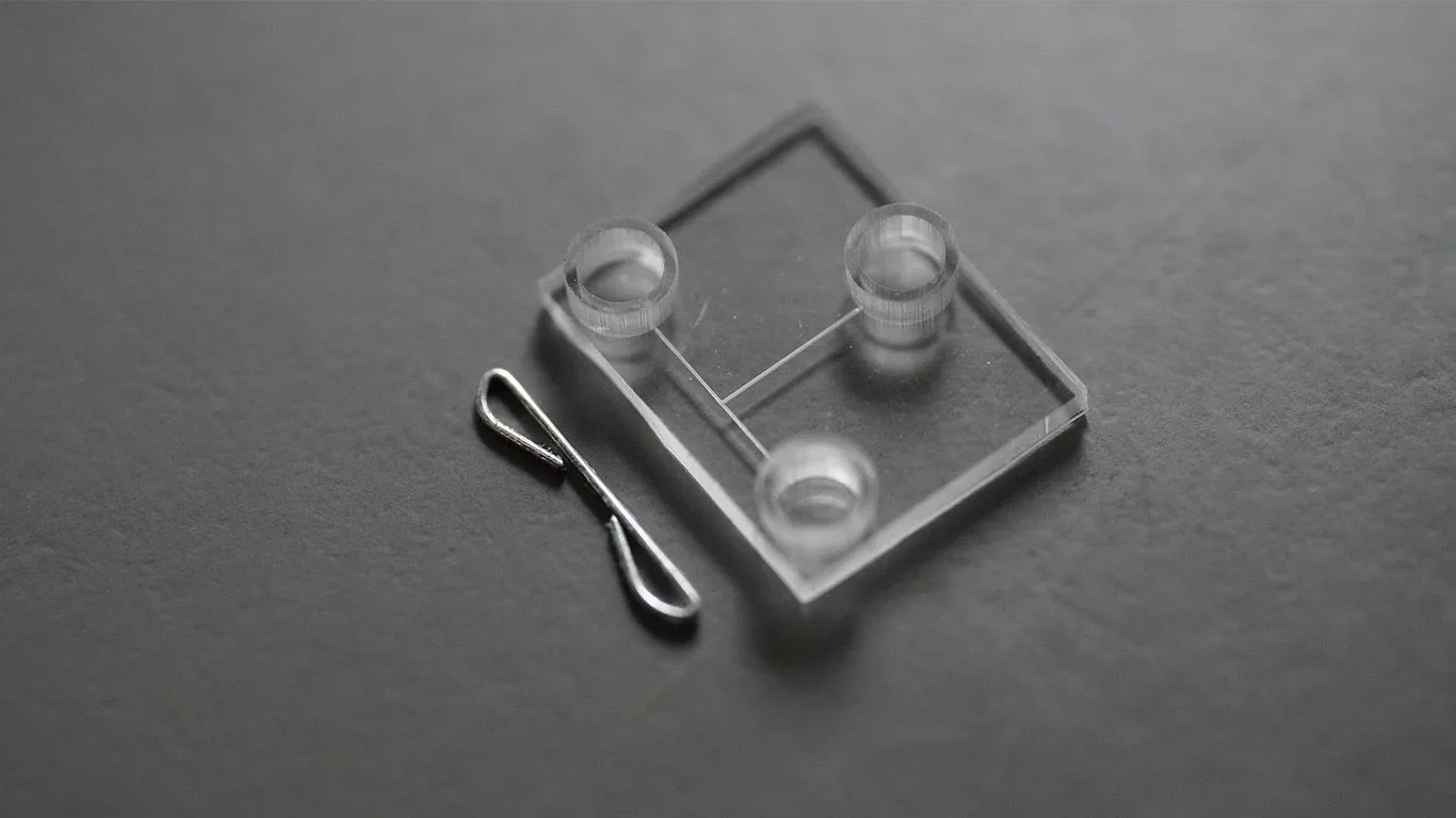 Microfluidic device printed in resin beside a standard staple, 12.7 mm across and 0.5 mm thick, for scale