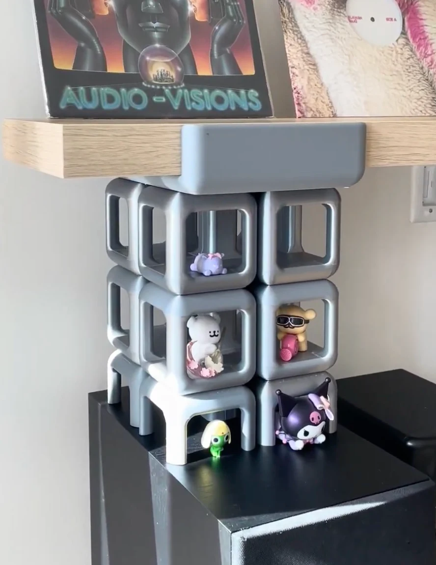 The real scale grey print on a speaker, holding up a record shelf, with small figures inside the cubes